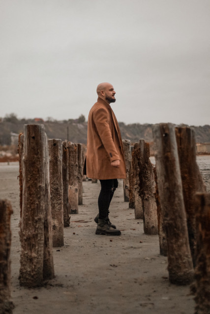 Contemplative Camel Coat Menswear Styling Reference Set on a Muted Urban-Rugged Landscape